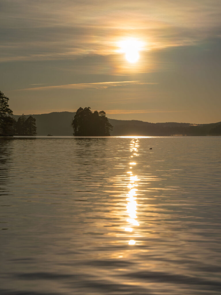 Solnedgång över Laxsjön i Dalsland med gyllene ljusreflex i vattnet och skogbevuxna öar i siluett.