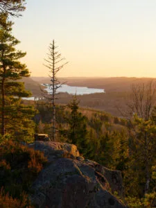 Utsikt från Åmålsberget vid solnedgång med barrskog, klippor och en speglande sjö i dalgången nedanför.