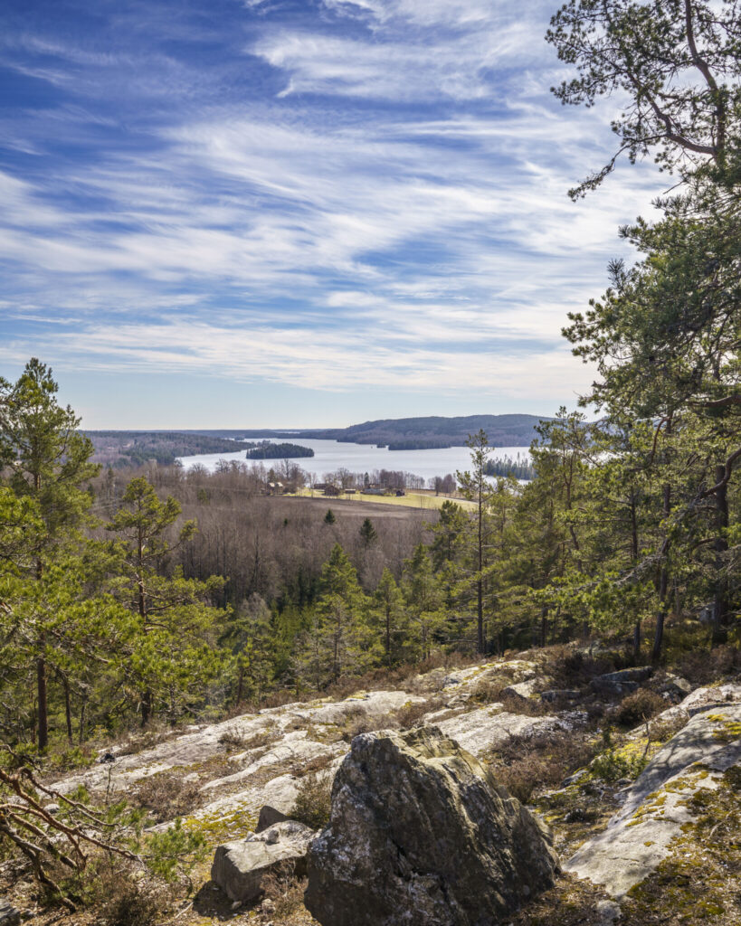Utsikt från berget Bläsen över sjö och skogslandskap i Dalsland, med klipphällar i förgrunden och tallar som ramar in vyn