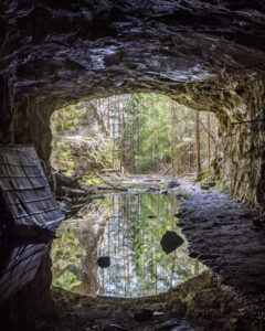 Vy inifrån stora gruvgången på Bläsen med stilla vattenspegel och utsikt mot grön barrskog, längs Bläsenrundan vid Fröskog i Dalsland