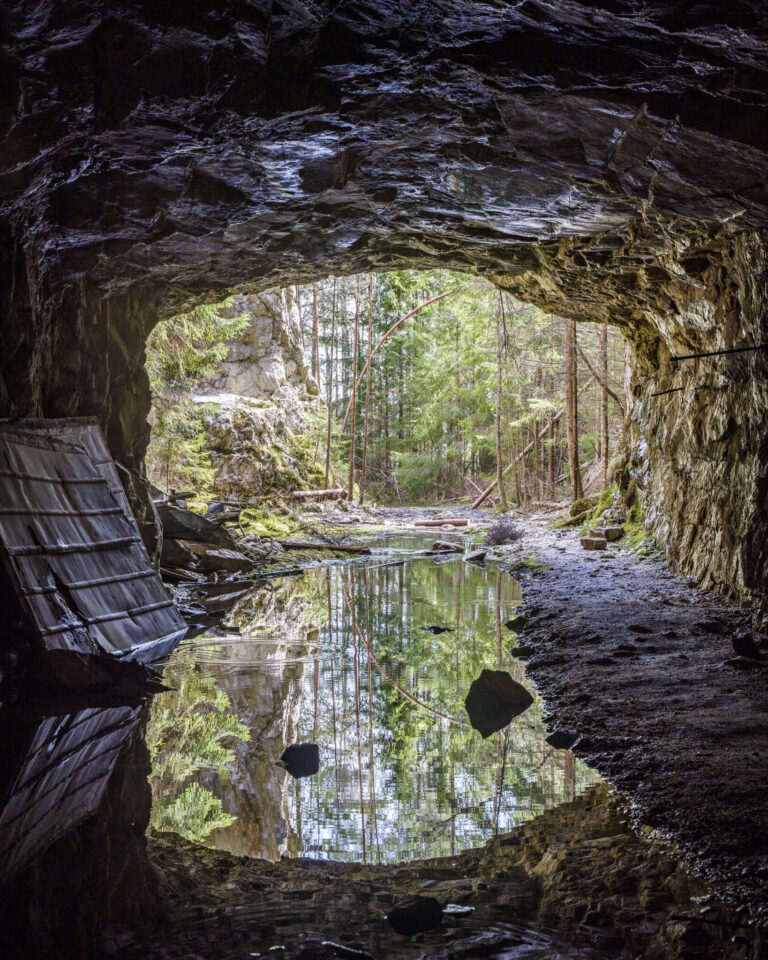 Vy inifrån stora gruvgången på Bläsen med stilla vattenspegel och utsikt mot grön barrskog, längs Bläsenrundan vid Fröskog i Dalsland