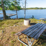 Piknikbänkar vid Trehörnabadet med bryggor och sjöutsikt en solig dag i Ödeshögs kommun, Östergötland