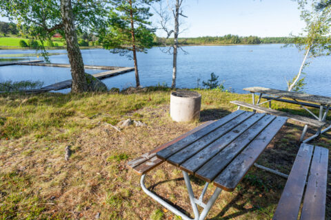 Piknikbänkar vid Trehörnabadet med bryggor och sjöutsikt en solig dag i Ödeshögs kommun, Östergötland
