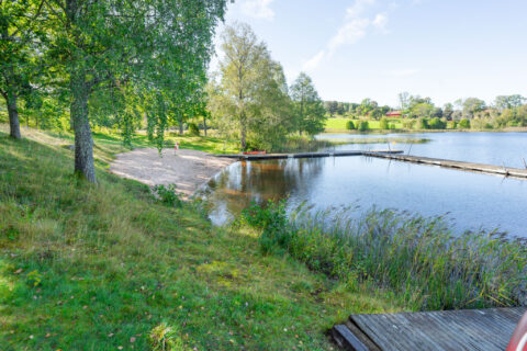 Trehörnabadet med sandstrand, badbryggor och grönskande björkar vid sjön en solig sommardag i Ödeshögs kommun