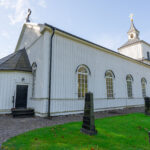 Vitmålad Trehörna kyrka i Östergötland, en träkyrka från 1861 med rundade fönster, klocktorn och omgivande kyrkogård.