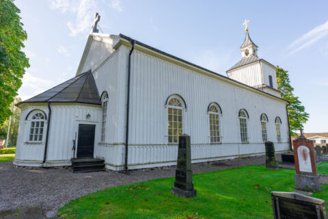 Vitmålad Trehörna kyrka i Östergötland, en träkyrka från 1861 med rundade fönster, klocktorn och omgivande kyrkogård.