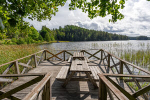 Träbrygga med picknickbord vid Klintens badplats, med utsikt över Vagnsjön omgiven av barrskog i Ödeshögs kommun.