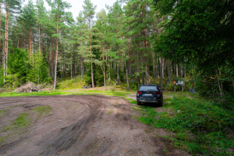 Parkering vid Ödemark naturreservat med en bil intill informationsskylt, omgiven av barrskog med tallar och granar i grön sommarmiljö