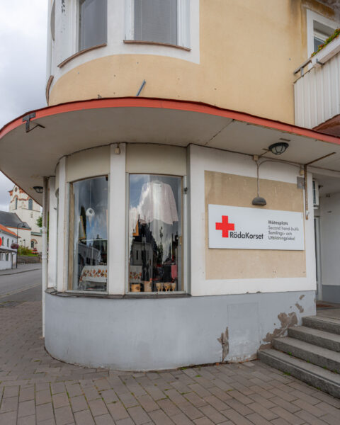 Röda Korsets second hand-butik i ett rundat hörnhus i Ödeshög, med skyltfönster och skylt för mötesplats och samlingslokal.