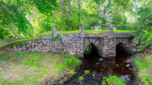 Gammal stenbro från 1700-talet vid Svämb i Ödeshögs kommun, omgiven av frodig grönska och en stilla bäck