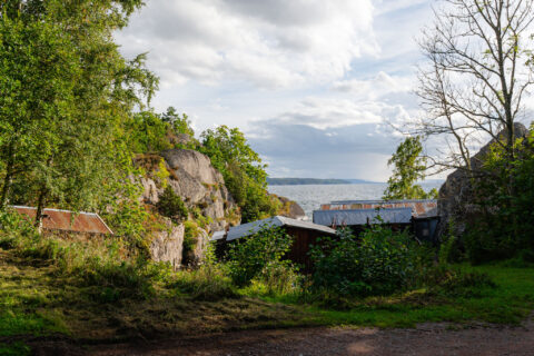 Klippor och små byggnader vid Öninge hamn med utsikt över Vättern, omgivna av grönska och lövträd i Ödeshögs kommun.