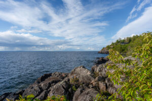 Klippig kust vid Öninge hamn längs Vättern med grönska, dramatisk himmel och en byggnad på udden i bakgrunden