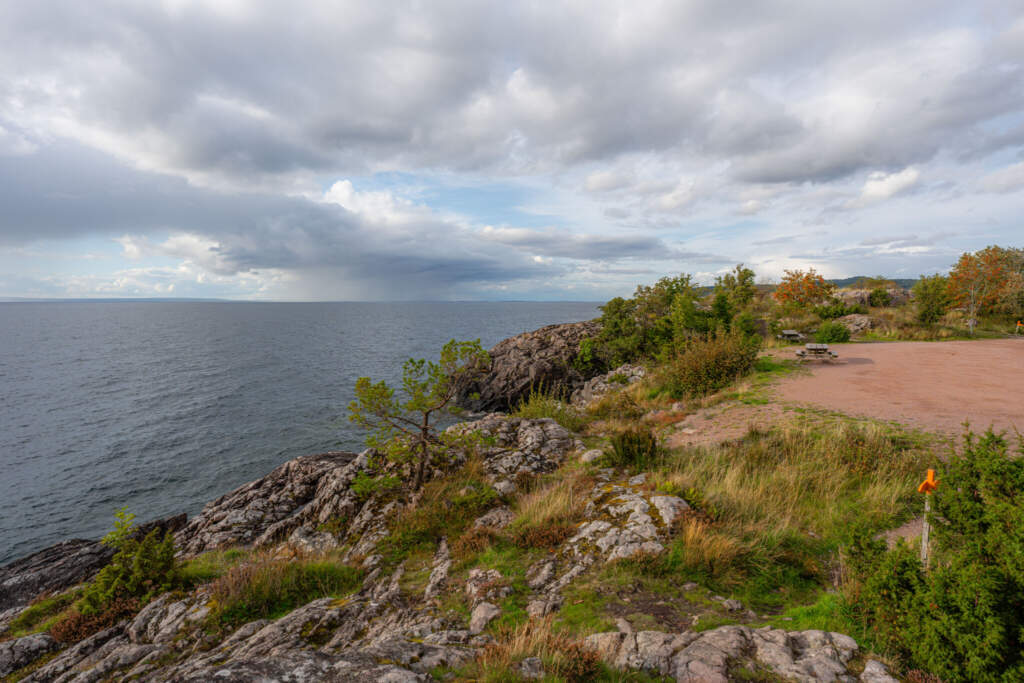 Klippig utsiktsplats vid Stora Lunds naturreservat med vidsträckt vy över Vättern, dramatisk molnhimmel och orange ledmarkering längs vandringsstigen.