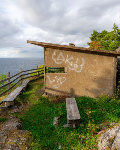 Vindskydd med graffiti och träbänkar vid klippkanten med utsikt över Vättern i Stora Lunds naturreservat, Ödeshög