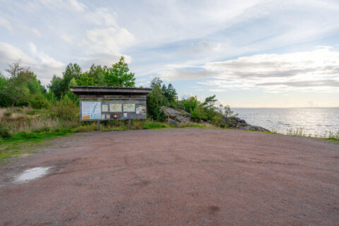 Informationstavla vid parkeringen i Stora Lunds naturreservat med rödaktig grusplan, klippor och utsikt över Vättern