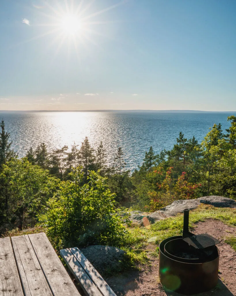 Grillplats och sittbänk vid Kråkeryds utsiktsplats med panoramavy över Vättern i solsken, omgiven av grönska och klippor