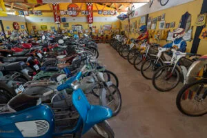 Samling av veteranmopeder och motorcyklar i Vadstena MC & traktormuseum, med skyltar och racingmemorabilia på väggarna