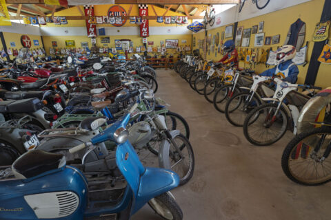 Samling av veteranmopeder och motorcyklar i Vadstena MC & traktormuseum, med skyltar och racingmemorabilia på väggarna