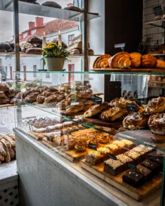 Glasdisk fylld med nybakade kanelbullar, croissanter, kakor och bröd på Bageri Hamilton i Vadstena, med vita stadshus synliga genom fönstret