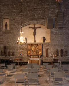 Interiör i Vadstena Klosterkyrka med medeltida krucifix, förgyllt altarskåp, stenväggar, kristallkrona och vita stolar
