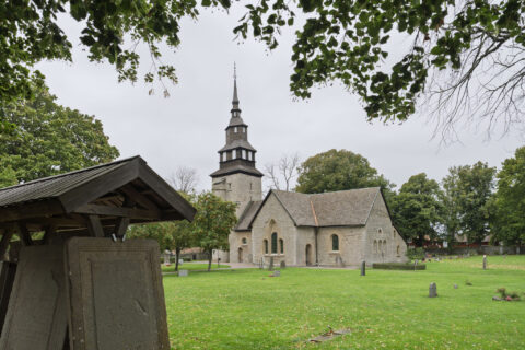 Medeltida Örberga kyrka i sten med spetsigt torn, omgiven av kyrkogård och grönska, en mulen dag i Östergötland