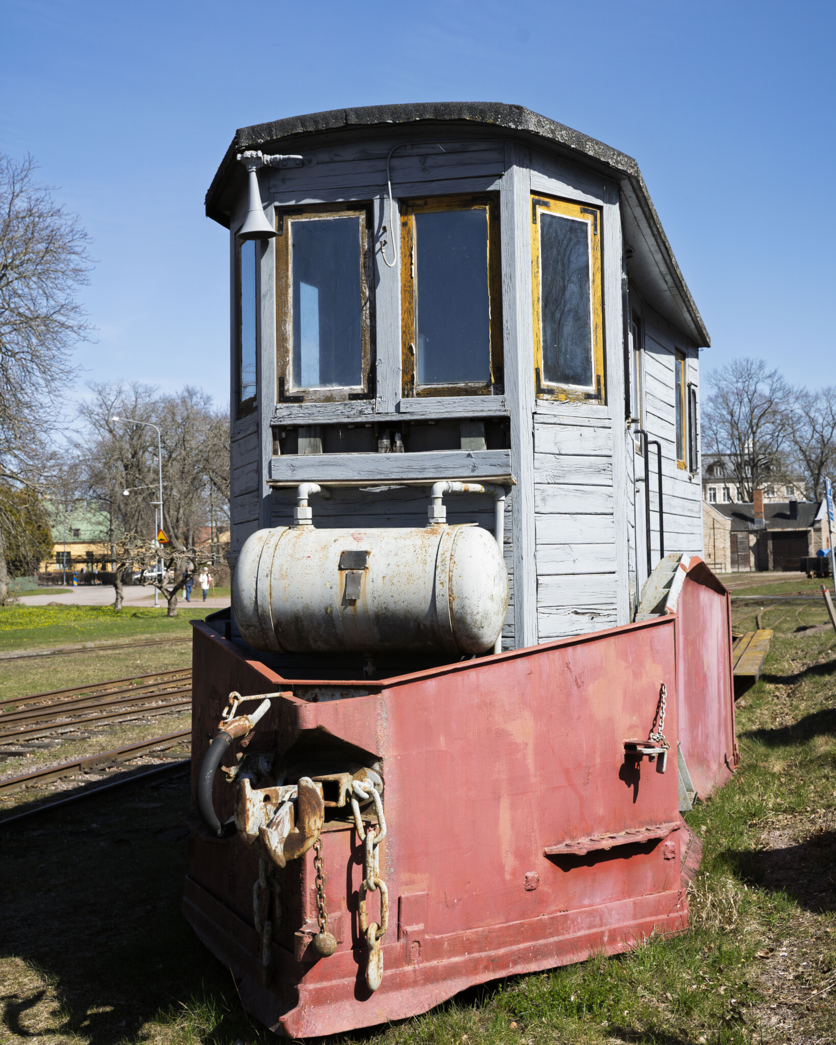 Gammalt smalspårigt lok med röd front och grå trähytt vid Wadstena-Fogelsta Järnväg i Vadstena, en solig vårdag