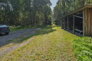 Parkering vid Ycke urskog med grusplan, parkerad bil och öppen rastplats under tak med bänkbord, omgiven av lummig lövskog.