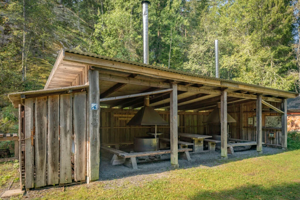 Öppen grillplats med tak, sitzbänkar och skorstenar i Ycke urskog, omgiven av lummig skog i Östergötland