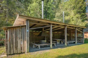 Öppen grillplats med tak, sitzbänkar och skorstenar i Ycke urskog, omgiven av lummig skog i Östergötland