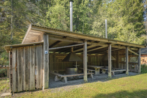 Öppen grillplats med tak, sitzbänkar och skorstenar i Ycke urskog, omgiven av lummig skog i Östergötland