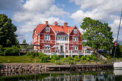 Göta Hotell i Borensberg, ett klassiskt rött trähotell med vita detaljer och veranda, beläget vid Göta kanals vattenspegel omgivet av grönska.