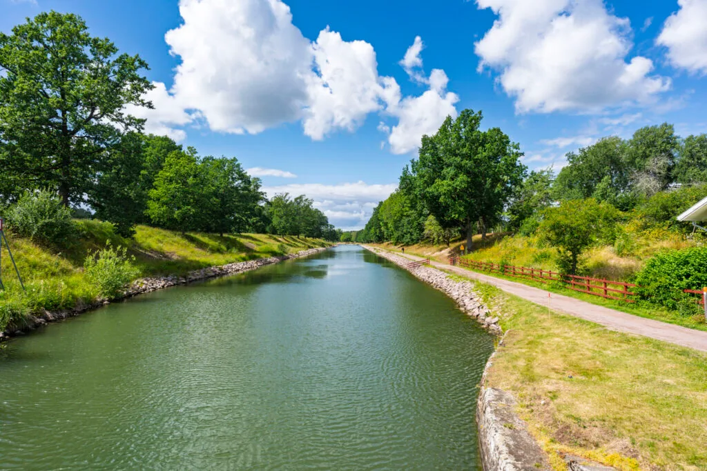 Göta kanal vid Nås nära Borensberg en solig sommardag med gångväg längs kanalen, gröna träd och vita moln på blå himmel
