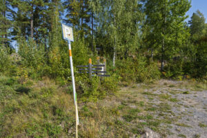 Parkeringsskylt och vägvisare vid en skogsväg längs Östgötaleden nära Amundebo, omgiven av björk och tall en sommardag.