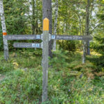 Vägvisare i skogen vid Östgötaleden med skyltar mot Drögenslingan, Drögen och parkering, omgiven av björkar och grönska.