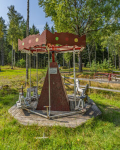 Gammal handdriven karusell med trähästar och färgglatt tak i skogsmiljö längs Amundeboslingan, Östgötaleden