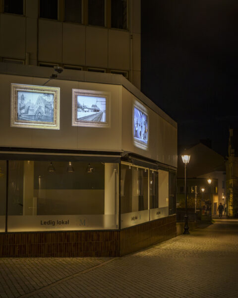 Kvällsbelyst hörnbyggnad med skylten "Ledig lokal" och projicerade historiska fotografier på fasaden, del av Vinterljus-evenemanget i Linköping.