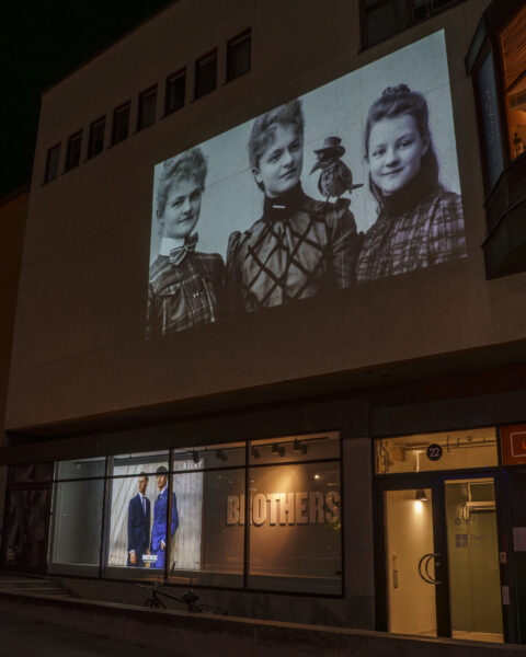 Historiskt svartvitt fotografi projicerat på en husfasad ovanför Brothers-butiken under Vinterljus i Linköping, kvällstid.