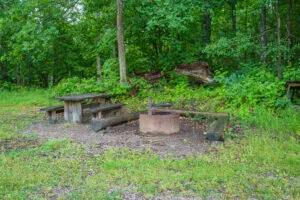 Rastplats vid Hovetorps slussar med träbänkar, bord och grillplats i murad eldstad, omgiven av grön lövskog längs Östgötaleden.
