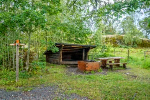 Vindskydd i trä med grillplats och sittbänk vid Hovetorps slussar längs Östgötaleden, omgivet av lummig grönska