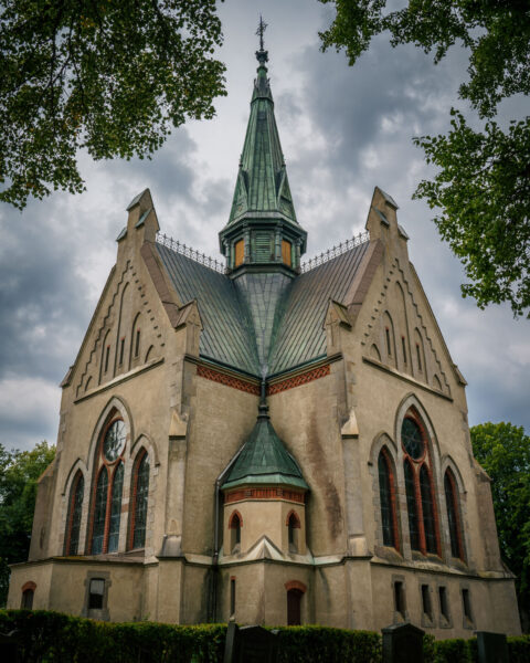 Orlunda kyrka i Vadstena kommun, en nygotisk kyrka ritad av Carl Möller med spetsig tornspira och grönt koppartak, omgiven av lövträd.