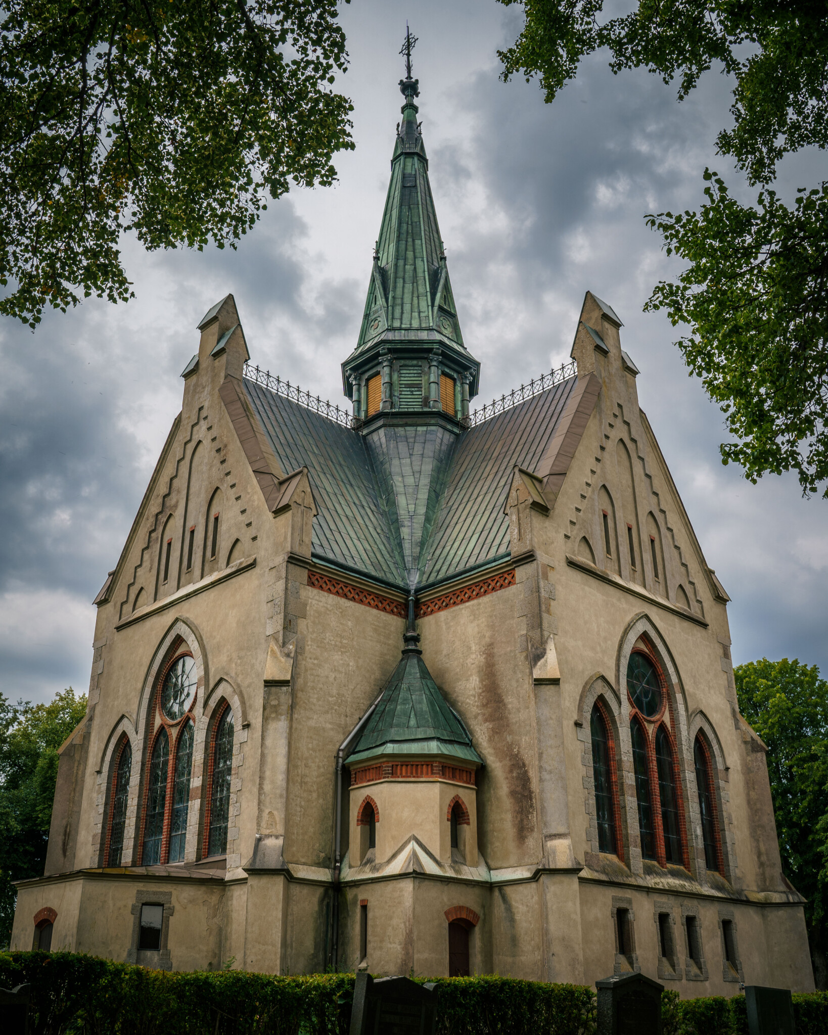 Orlunda kyrka i Vadstena kommun, en nygotisk kyrka ritad av Carl Möller med spetsig tornspira och grönt koppartak, omgiven av lövträd.