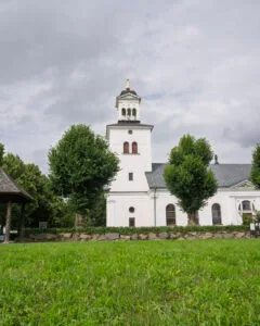 Röks kyrka i Ödeshögs kommun, en vitputsad empirekyrka från 1840-talet omgiven av gröna träd och gräsmatta under molnig himmel.