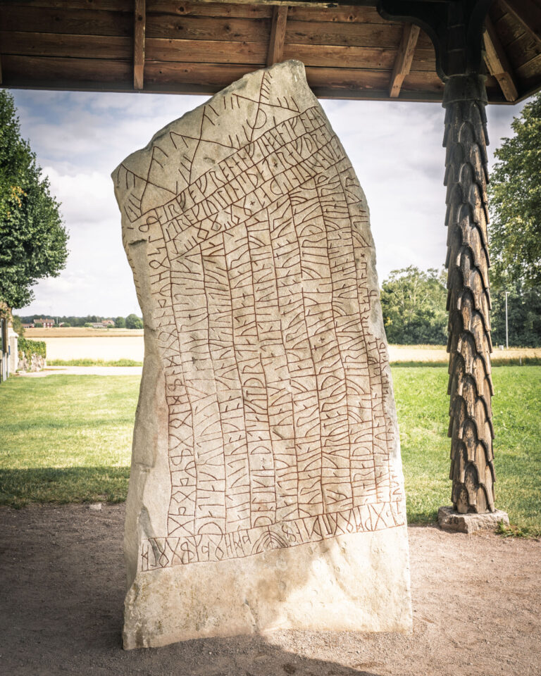 Rökstenen i Ödeshög, världens längsta kända runinskription med 760 runor, under ett skyddande trätak omgiven av grönska.