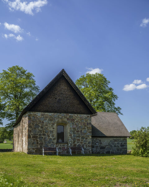 Hägerstad gamla kyrka, en medeltida stenkyrka från 1200-talet omgiven av gröna ängar och lövträd en solig sommardag i Kinda kommun.
