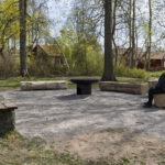Grillplats med stockbänkar och eldskål i parken vid Åtvidabergs Stora kyrka, en man sitter på en bänk omgiven av vårgrönska