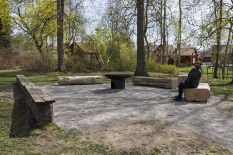 Grillplats med stockbänkar och eldskål i parken vid Åtvidabergs Stora kyrka, en man sitter på en bänk omgiven av vårgrönska
