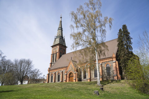 Åtvids Stora kyrka i nygotisk stil med tegelfasad och spetsigt torn, omgiven av grönska och björkar en vårdag i Åtvidaberg