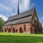 S:t Laurentii kyrka i Söderköping, medeltida tegelkyrka med trappgavel och hög spira omgiven av grön gräsmatta en solig dag