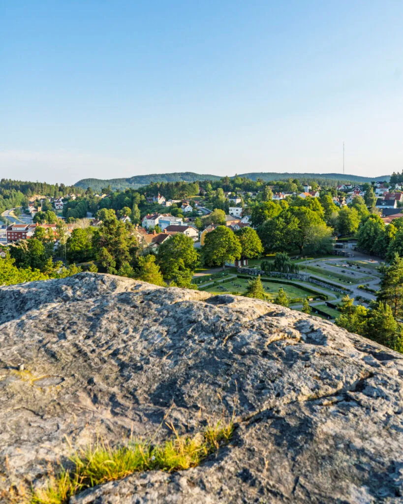 Utsikt från Borgarberget över Kisa samhälle med kyrkogård, grönskande träd och skogsklädda kullar i bakgrunden.
