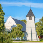 Drothems kyrka med vit trappgavel och fristående klockstapel omgiven av grönskande träd en sommardag i Söderköping
